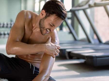 Young athletic man feeling pain in his shoulder while exercising in health club.