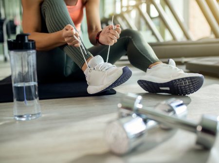 Unrecognizable female athlete tying shoelace while preparing for sports training in a gym.